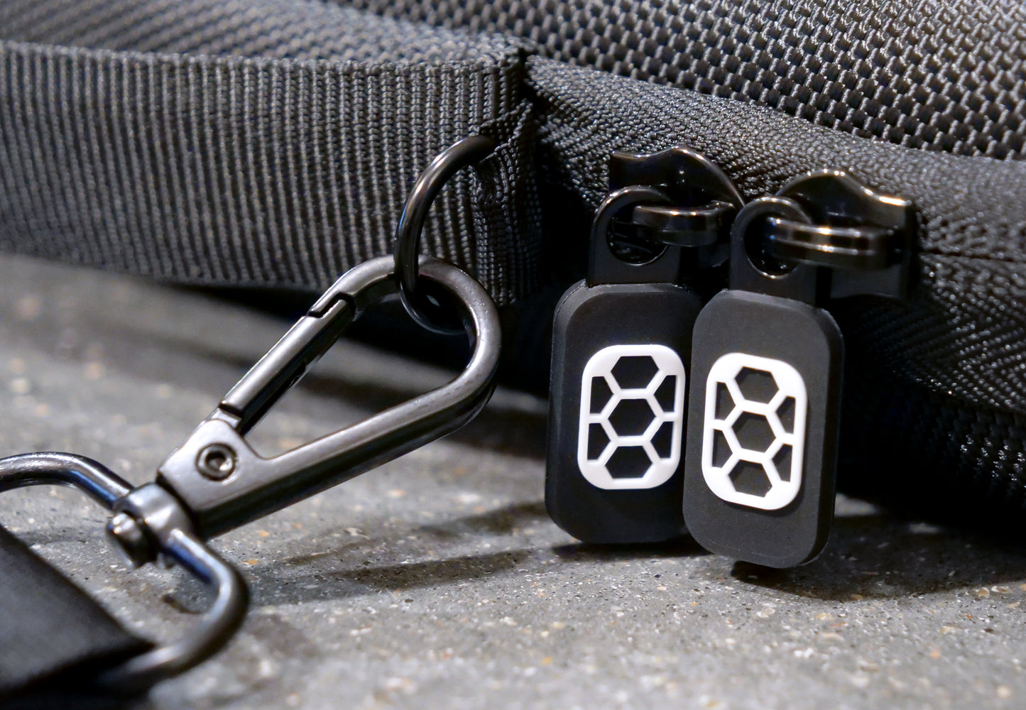 Black shoulder strap and D-Ring sewn into Comic Shell comic travel case, with dark metal hardware. Two black and white Comic Shell logo zipper pulls 